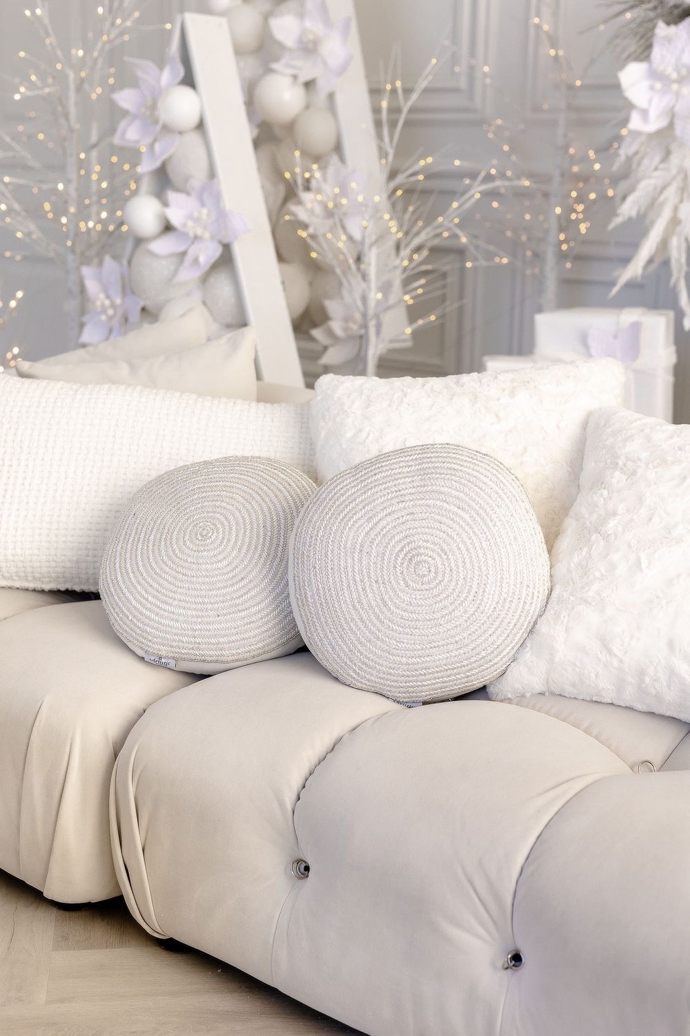 A cozy white tufted sofa with circular throw pillows and delicate floral decorations in soft purple and white.