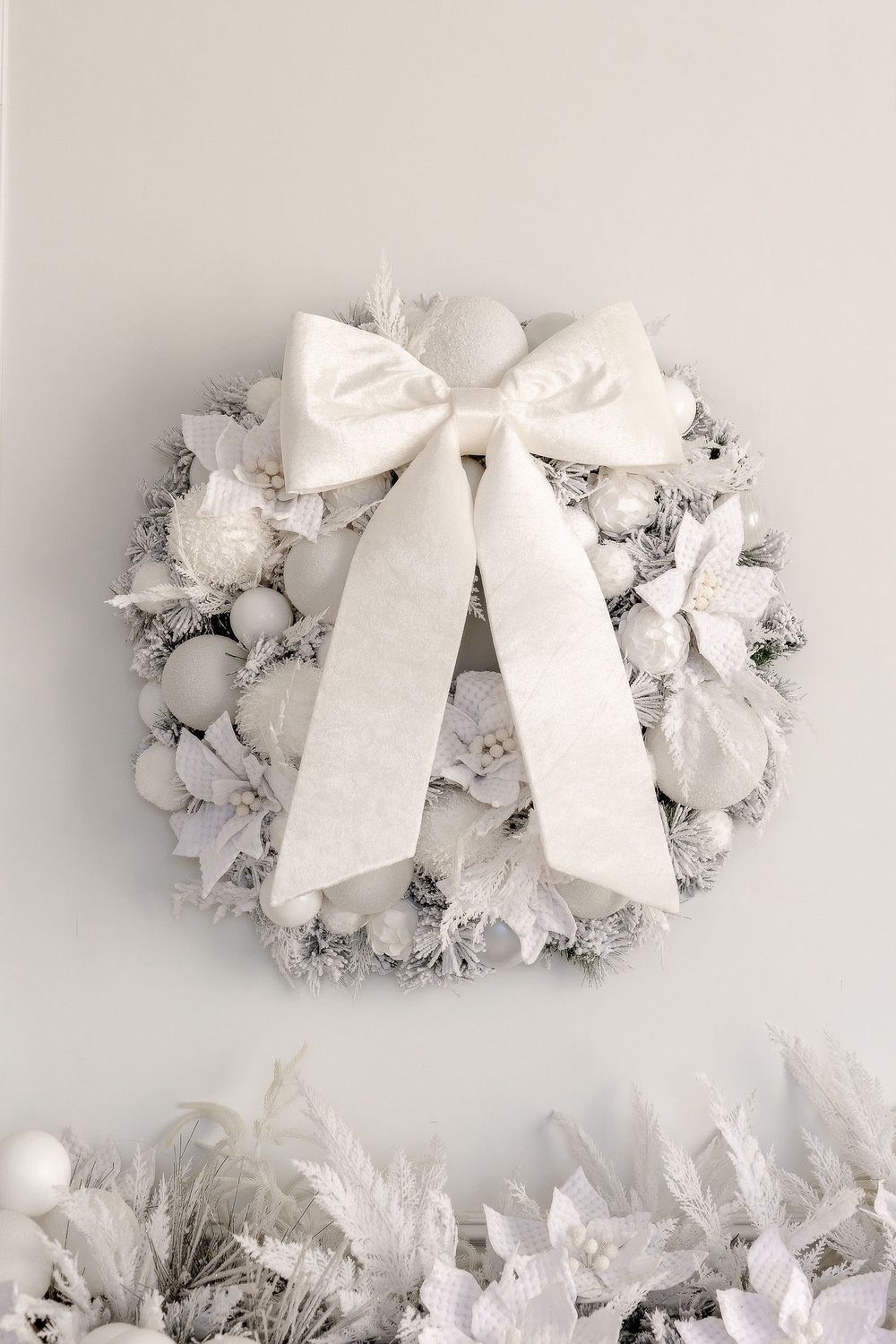 White wreath decorations with large bows mounted on a light colored wall create a minimalist holiday display.