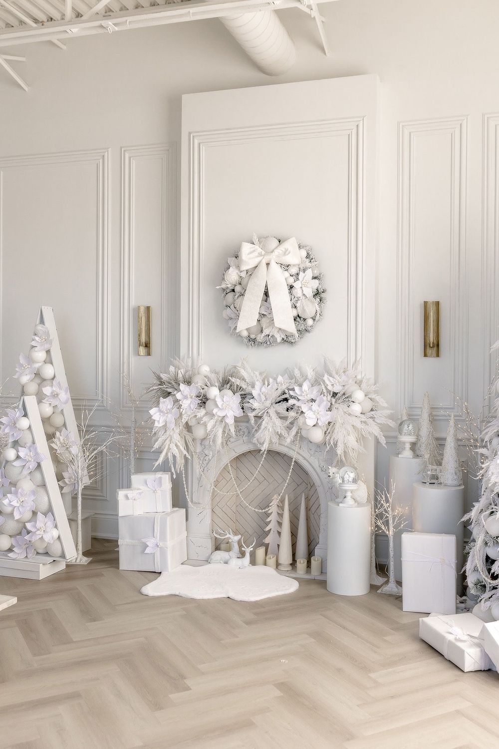 All-white Christmas decor featuring trees, wreaths and gifts arranged in an elegant room with paneled walls.