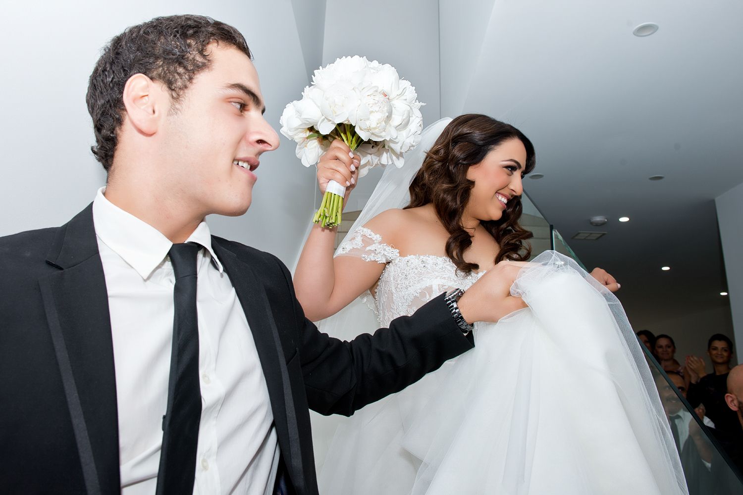 A joyful wedding celebration with a bride in white holding a bouquet while walking down a hallway.