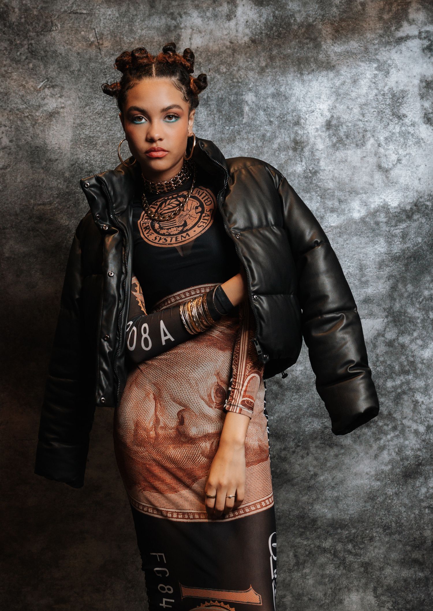 Fashion portrait in shades of brown and black featuring a statement necklace and leather jacket against textured backdrop.