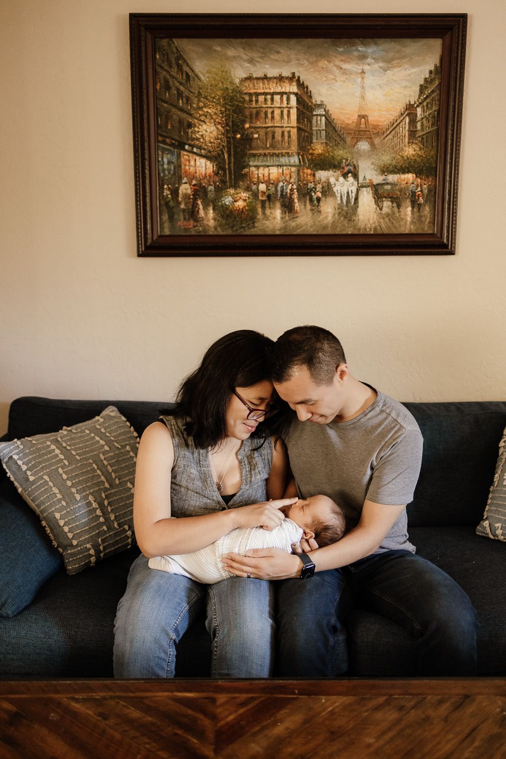 Proud parents holding baby on their living room sofa with a beautiful picture framed above - Bay Area newborn photography