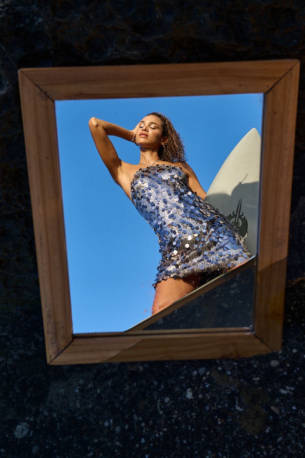 A dancer in a sparkly blue sequined dress strikes a graceful pose against a bright blue sky through a wooden frame.