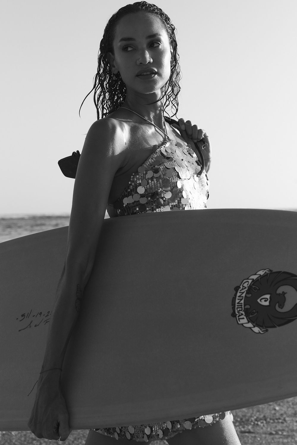 Black and white portrait of a surfer with wet hair holding a surfboard on a beach.
