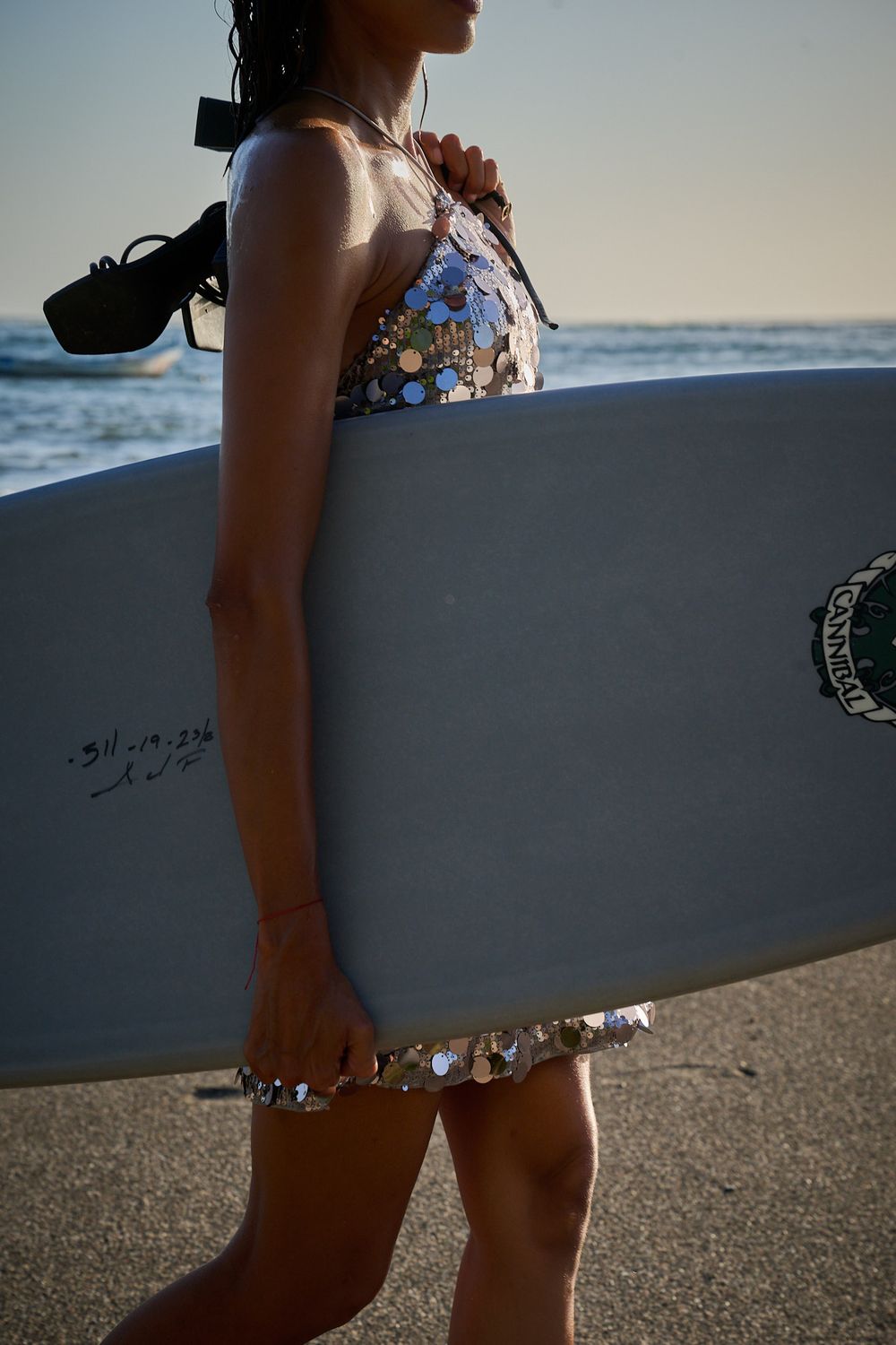 Side view of a surfer in floral swimwear standing on the beach with a surfboard at sunset.