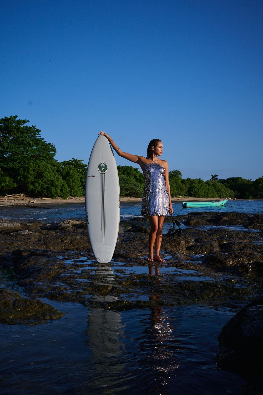 Sequence of a surfer walking across rocky shoreline at sunset with surfboard against vibrant blue sky and ocean.