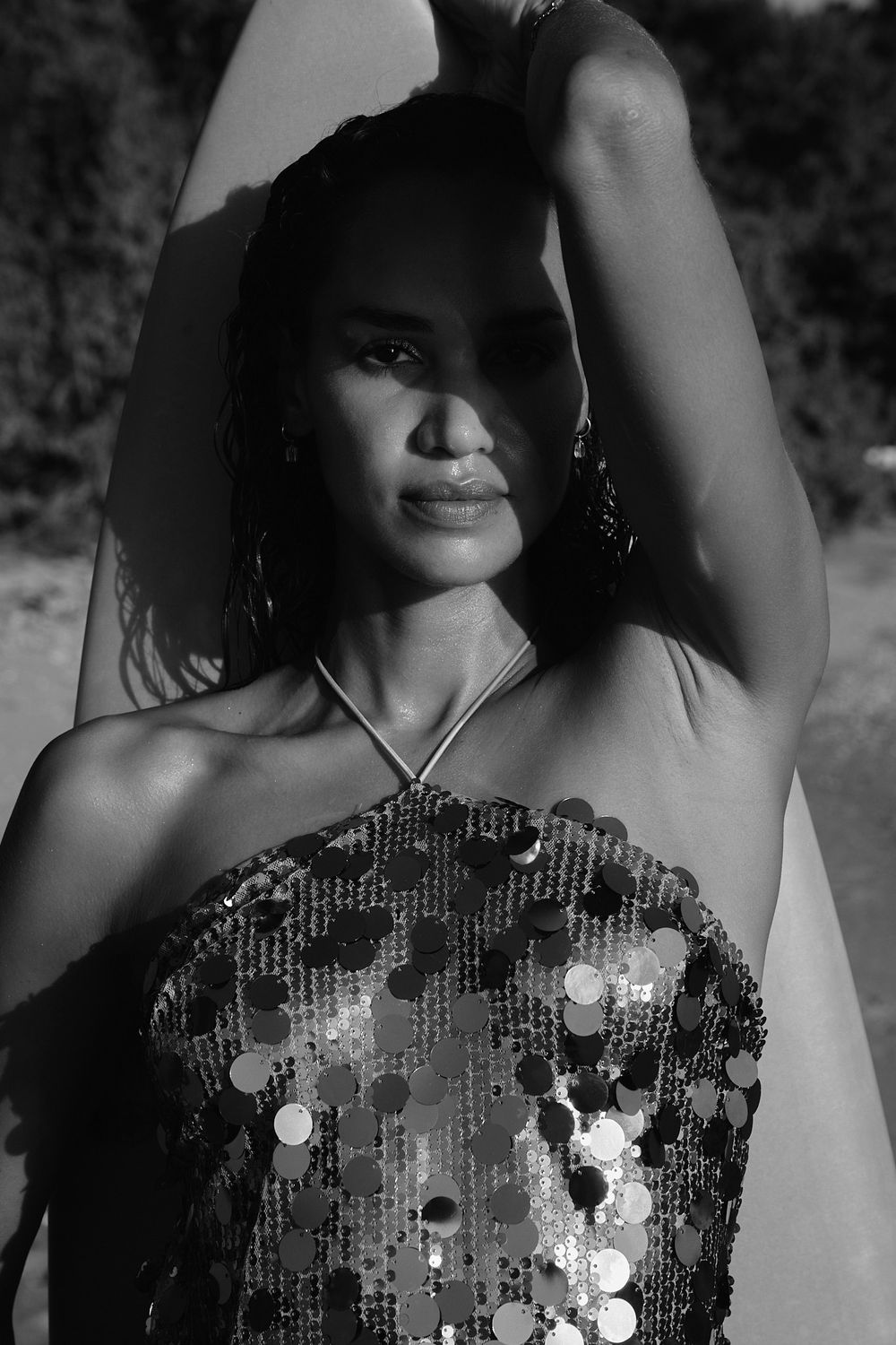 Black and white portrait of a person wearing a sequined strapless top posing with one arm raised.