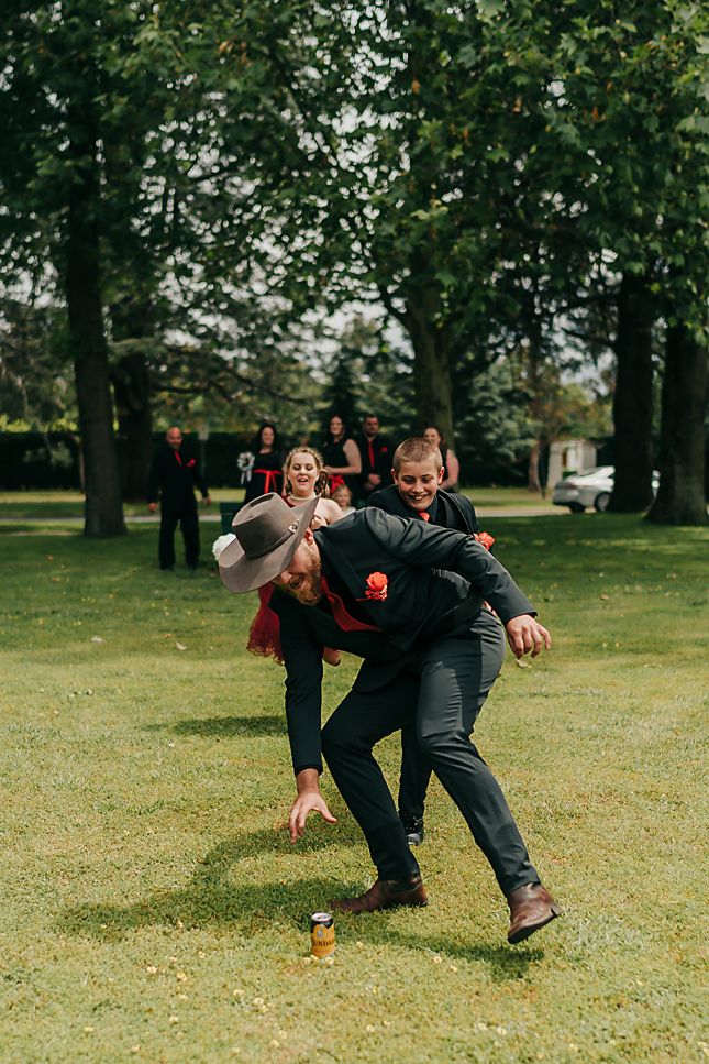 Wedding party groomsmen playfully tackle and pose on grassy lawn during outdoor photo session.
