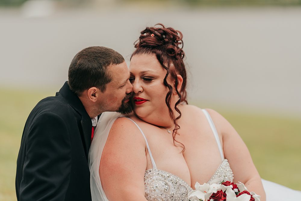 A romantic wedding moment captured outdoors as the groom whispers to the bride wearing a white lace dress.