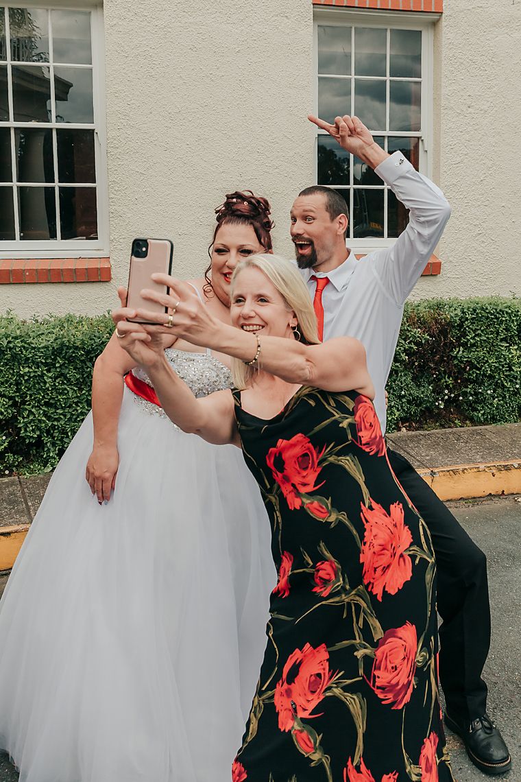 Group wearing formal attire and taking selfies together against a white building with windows.