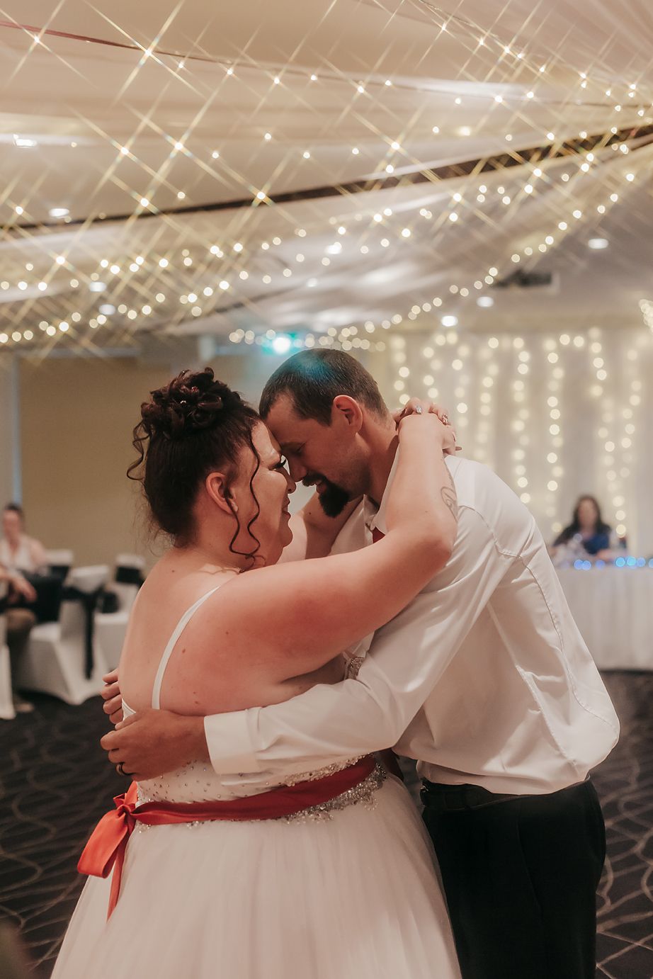 Couple sharing an intimate dance moment under twinkling string lights at their wedding reception.