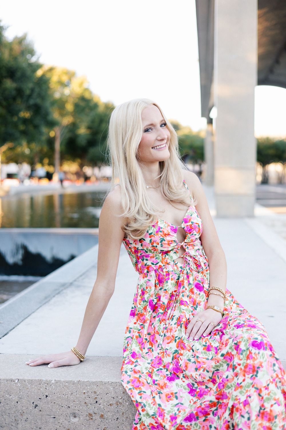 A person in a vibrant floral summer dress poses on white concrete steps in an outdoor setting.