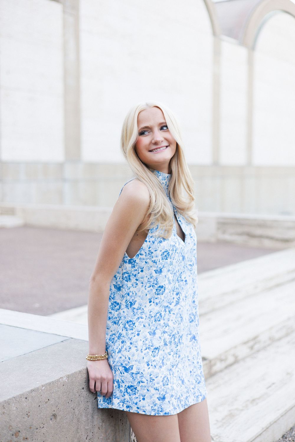 A summery blue and white floral dress is styled with delicate accessories in an architectural setting.