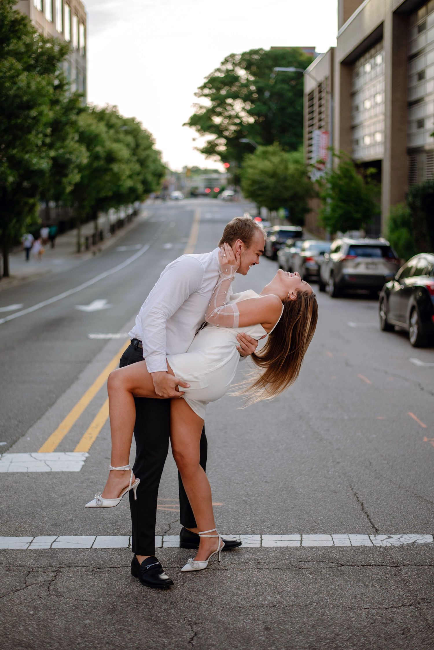 A romantic couple in formal wear sharing an intimate dip kiss on an urban street. Engagement photos in NC.