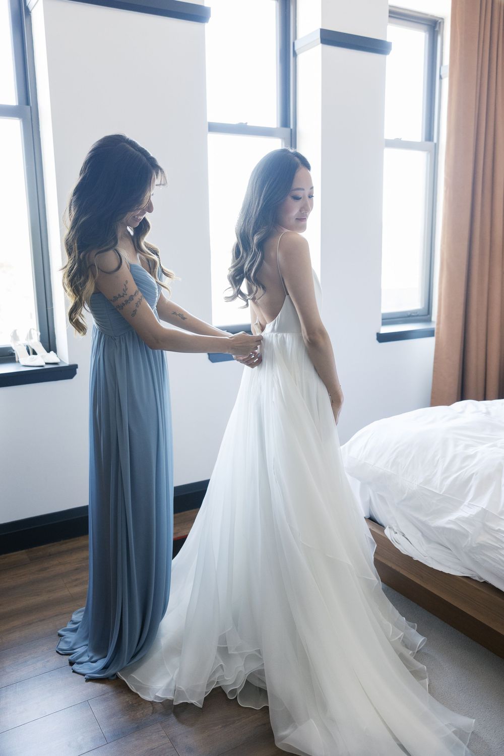 Wedding dress preparations in a sunlit hotel room with flowing white gown.