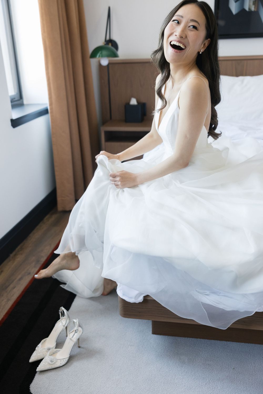 A joyful pre-wedding moment showing bright laughter while sitting on a modern bed.