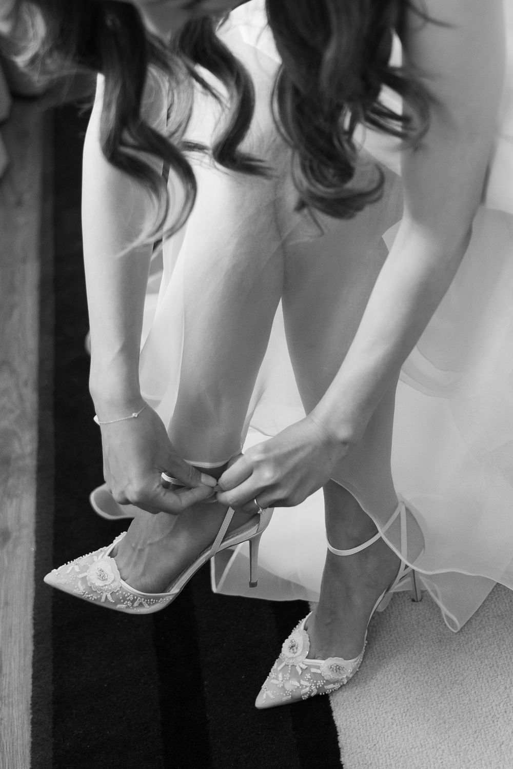 Close-up black and white photo of lace wedding shoes being fastened on a bride's feet.