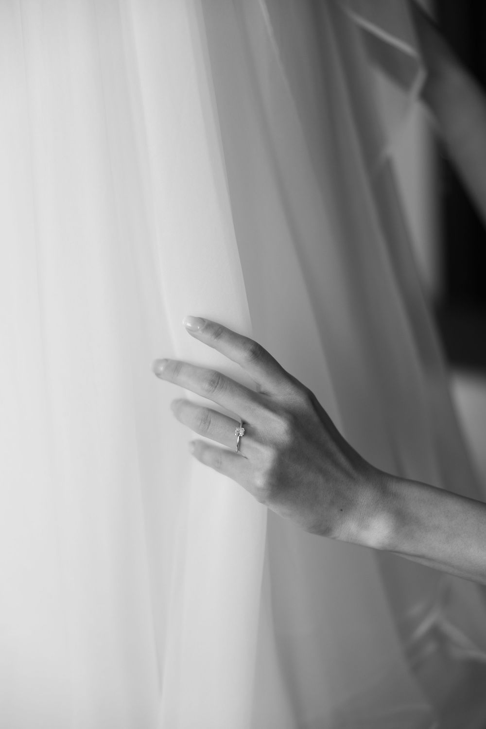 Close-up black and white photo of hands with engagement ring against flowing white fabric.