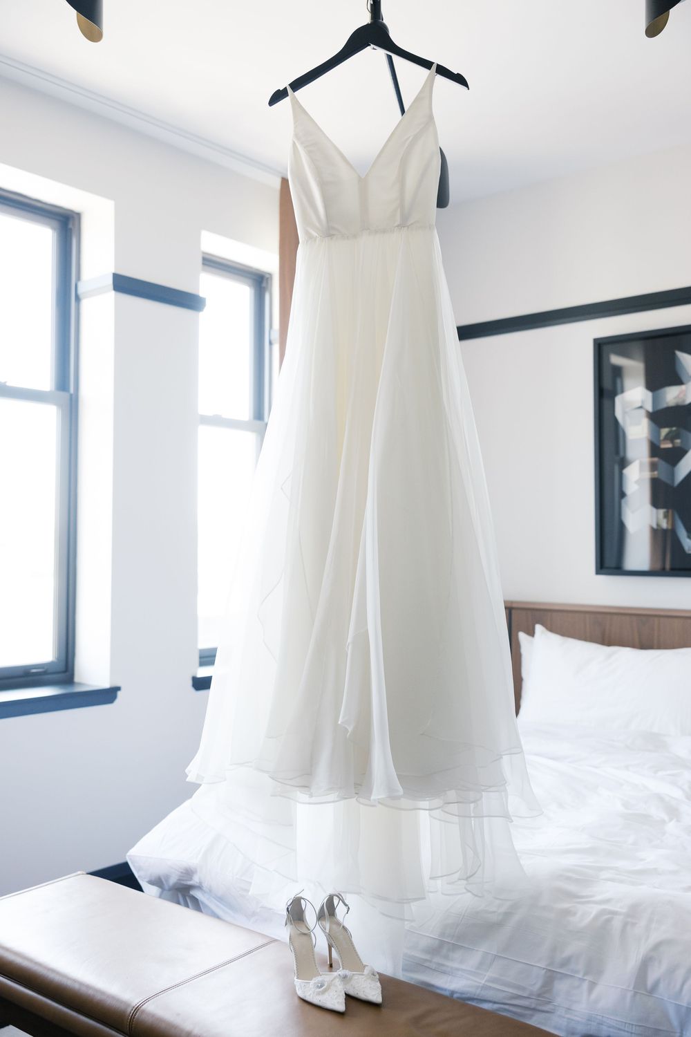 White wedding dress hanging in bright room with natural light streaming through windows.