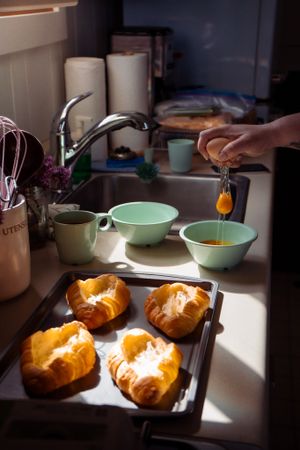 Fresh croissants on a baking tray while honey is being drizzled in mint green bowls.