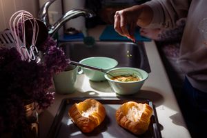 Honey being poured over freshly baked pastries in a sunlit kitchen scene.