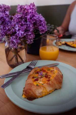 Breakfast plate with pastry served alongside purple lilac flowers and orange juice.