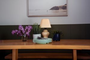 Minimalist table setting with purple flowers, stacked plates, and table lamp against dark wall.