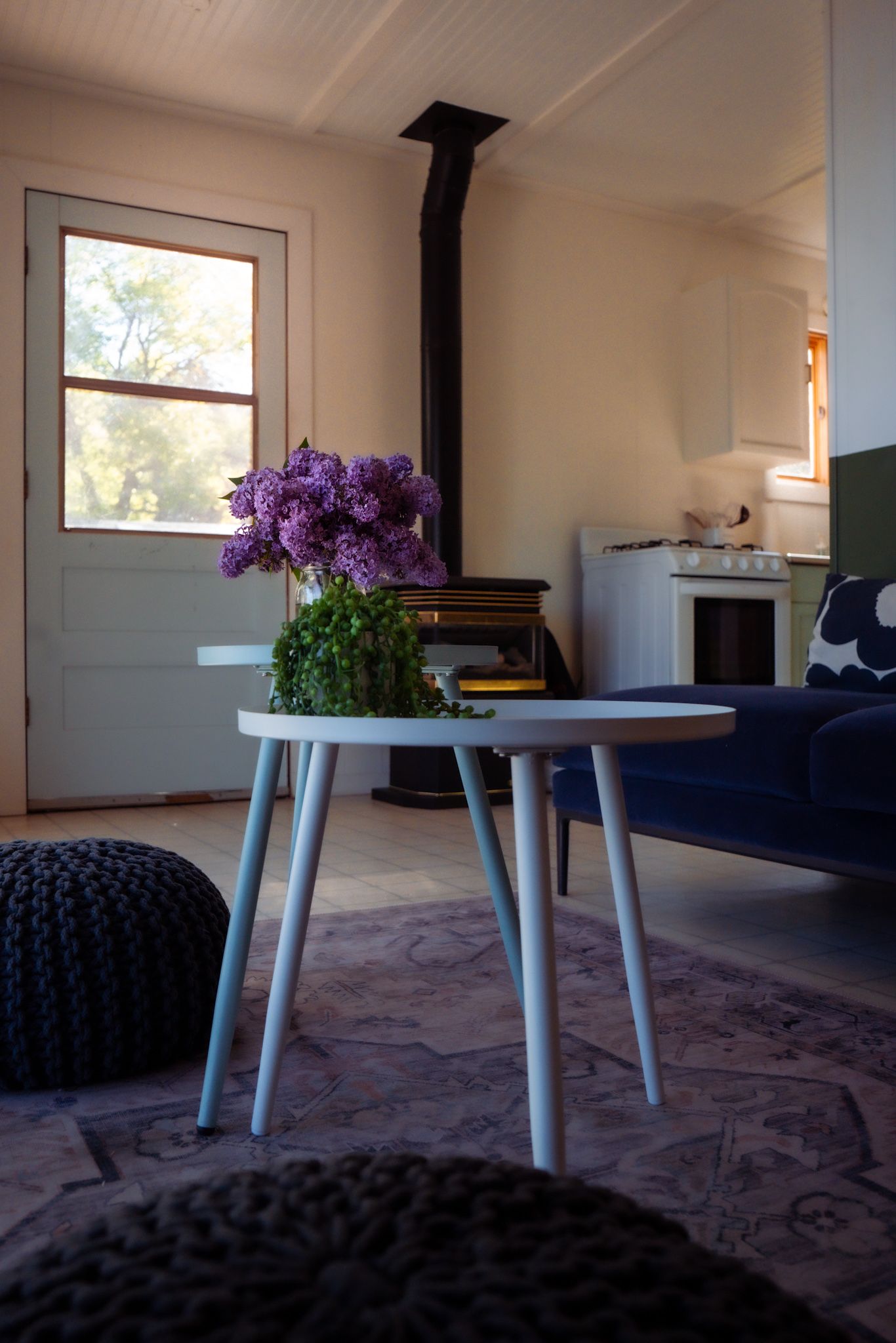 Purple flowers in a vase on a white table next to a blue couch in a modern living room.