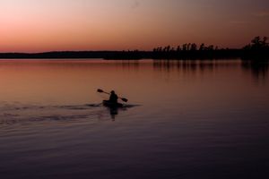Silhouette of a kayaker paddling across a tranquil lake during a pink sunset.