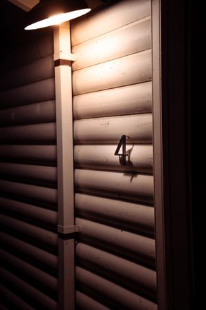 Illuminated lamp post casting light on white siding with number 4 mounted on wall.