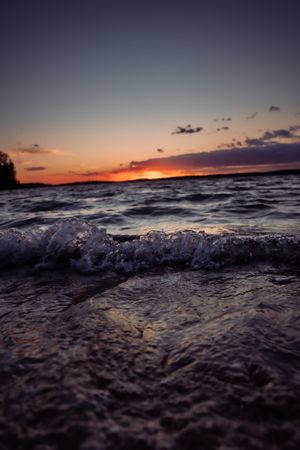 Dramatic sunset over choppy lake waters with waves crashing in the foreground.