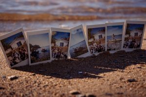A row of vintage polaroid photographs laid out on sandy beach ground showing vacation memories.