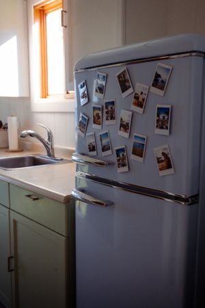 Vintage-style white refrigerator covered with polaroid photos in a mint green kitchen.