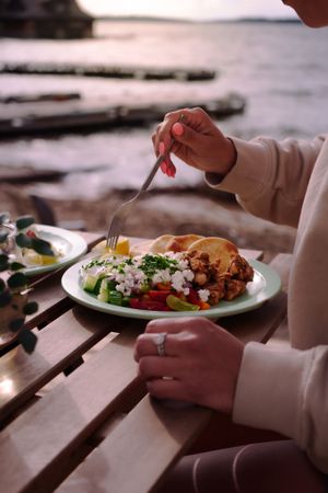 A plate of fresh food being eaten at an oceanside table during sunset.