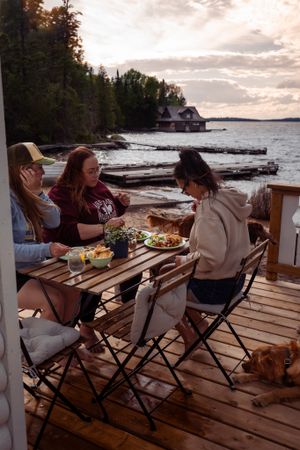Friends enjoying a meal together on a lakeside deck with a scenic waterfront view.