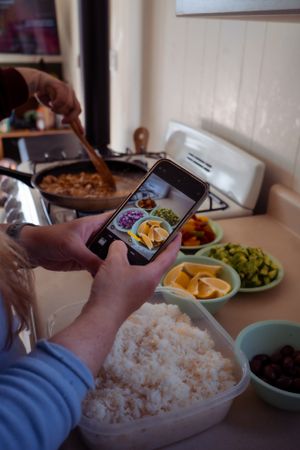 Someone taking food photos with smartphone while preparing a meal in kitchen.