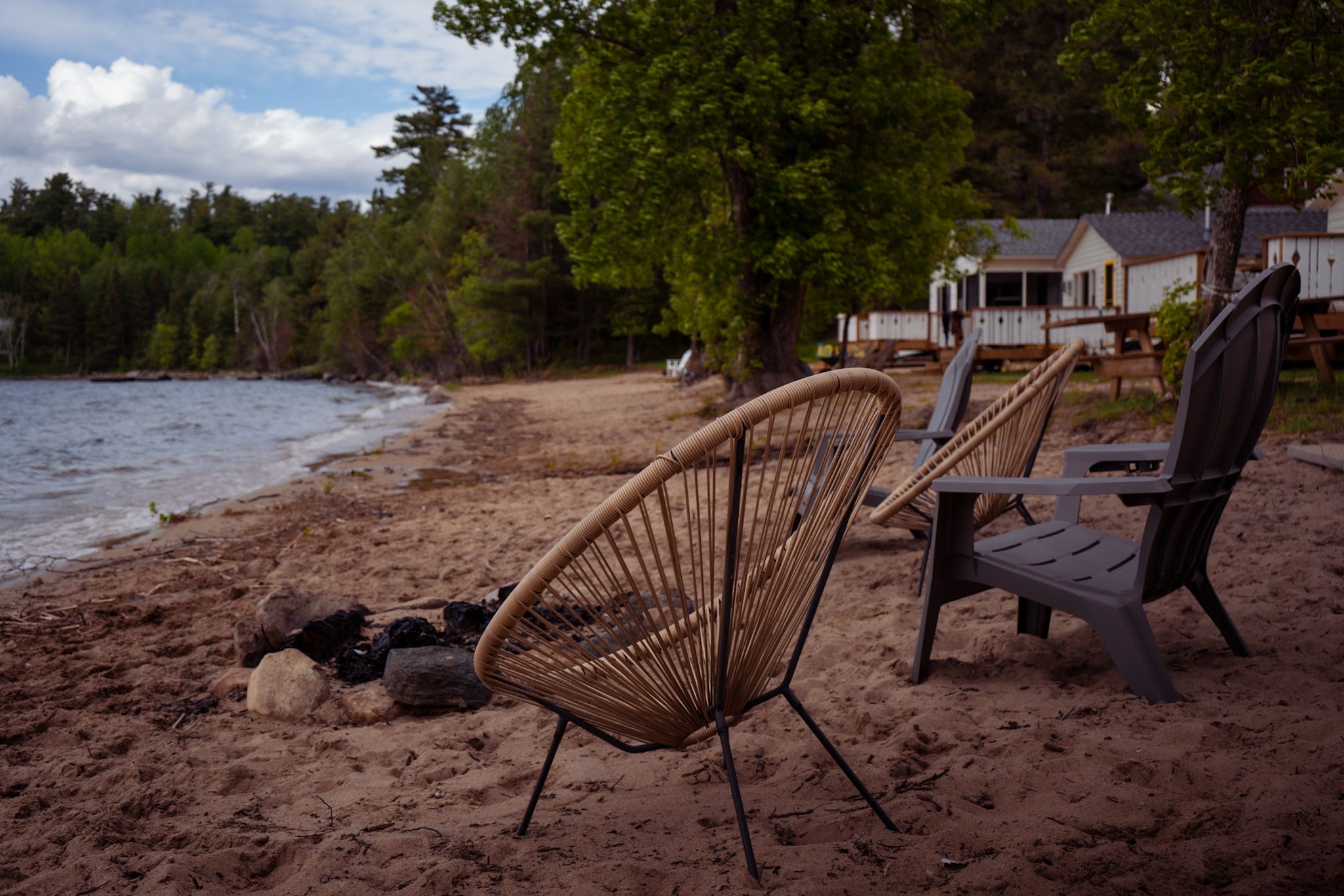Modern beach chairs arranged on a sandy lakefront with cottage in background.