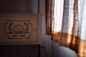 Sunlit window with sheer curtains next to decorative wall panel with shell design.