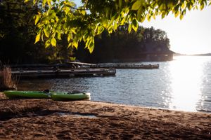 Serene lakeside beach with canoe under tree branches at sunset.