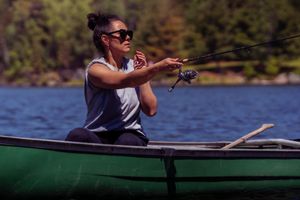 Person fishing from green canoe on tranquil lake surrounded by forest.