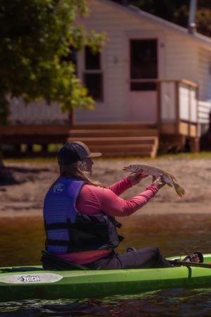 Kayaker in safety vest holding up caught fish while sitting in green kayak.