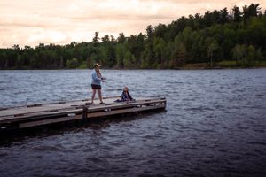 People relaxing on a wooden dock overlooking a serene lake surrounded by forest.