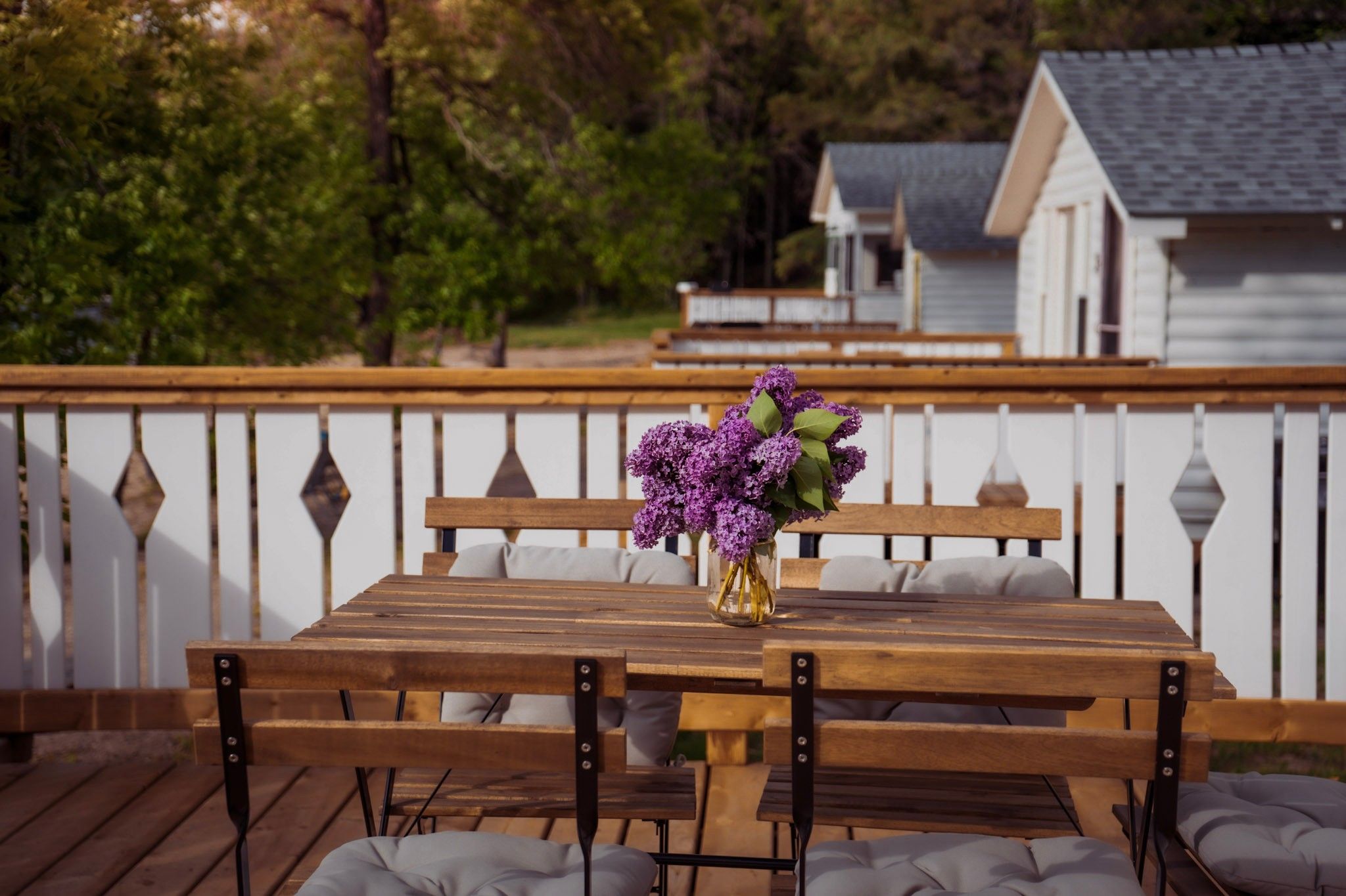 Rustic outdoor dining setup with wooden benches and purple flowers on a deck with decorative railing.