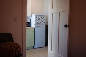 Interior view of a kitchen corner with a white refrigerator and sage green cabinets.