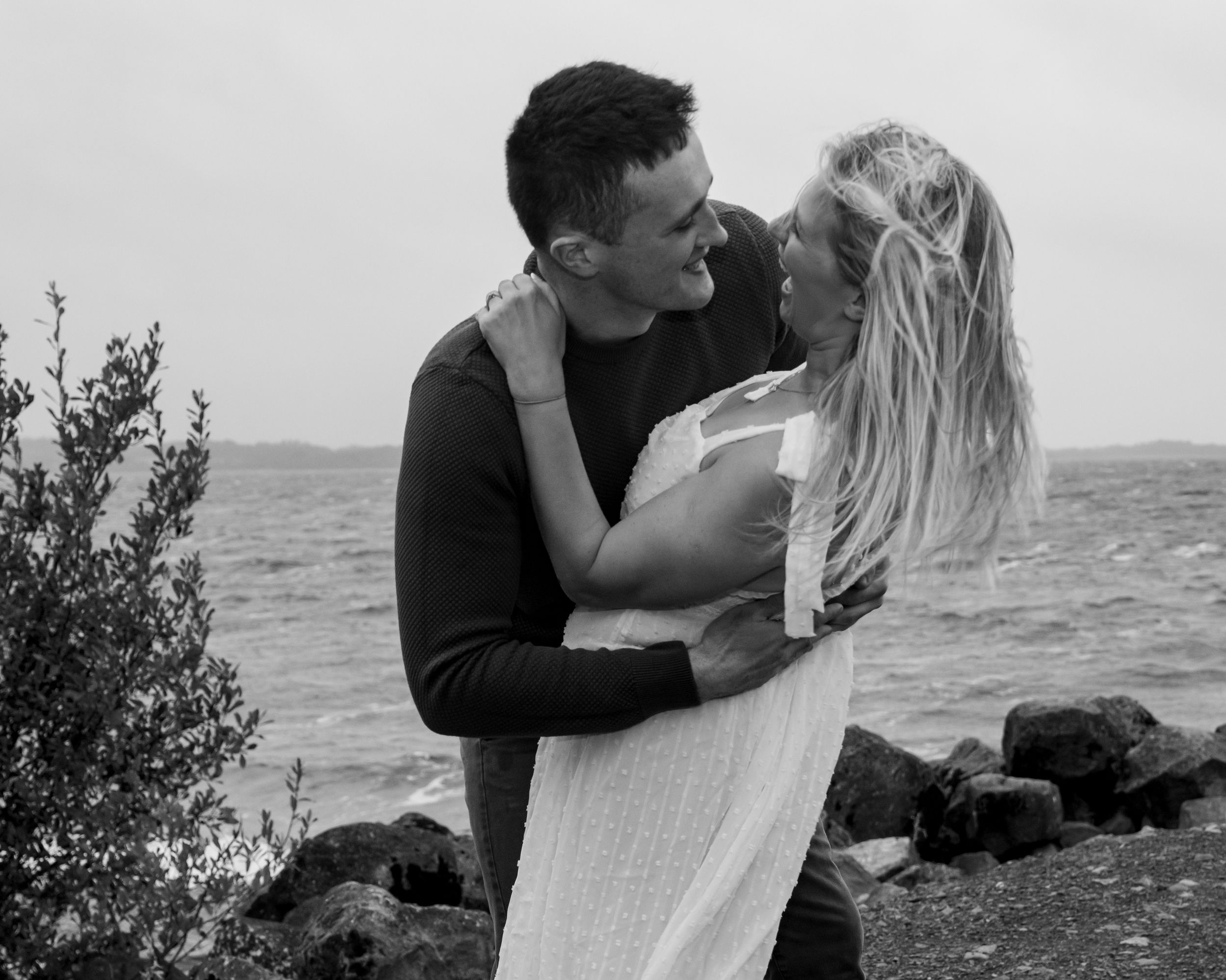 Black and white coastal photo series showing intimate moments between two people near the ocean.