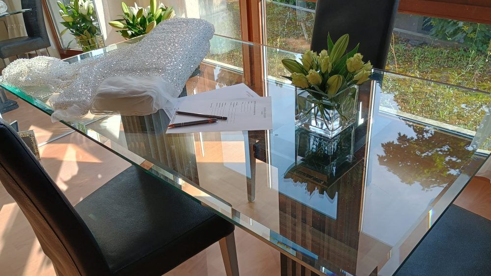 Glastisch mit Blumen und einer Stoffrolle aus glänzendem bestickten Stoff