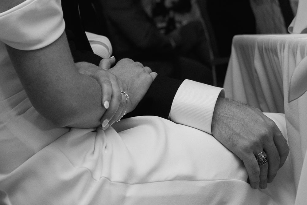 Close-up of bride and groom holding hands, wedding rings visible, black and white photo.