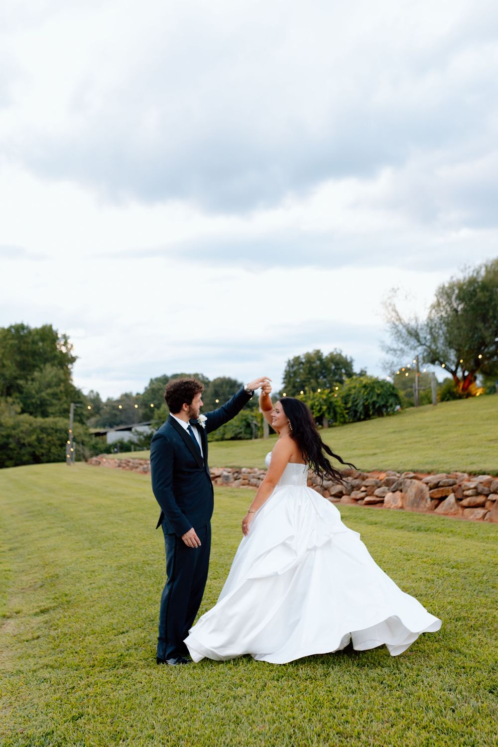 A bride and groom share a romantic dance on a lush green lawn during their outdoor wedding celebration.