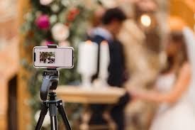 Smartphone on tripod recording a wedding ceremony with blurred couple exchanging vows in background.