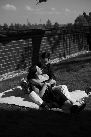 A couple snuggle on a picnic blanket following their engagement - she reclines in his arms and smiles up at him.